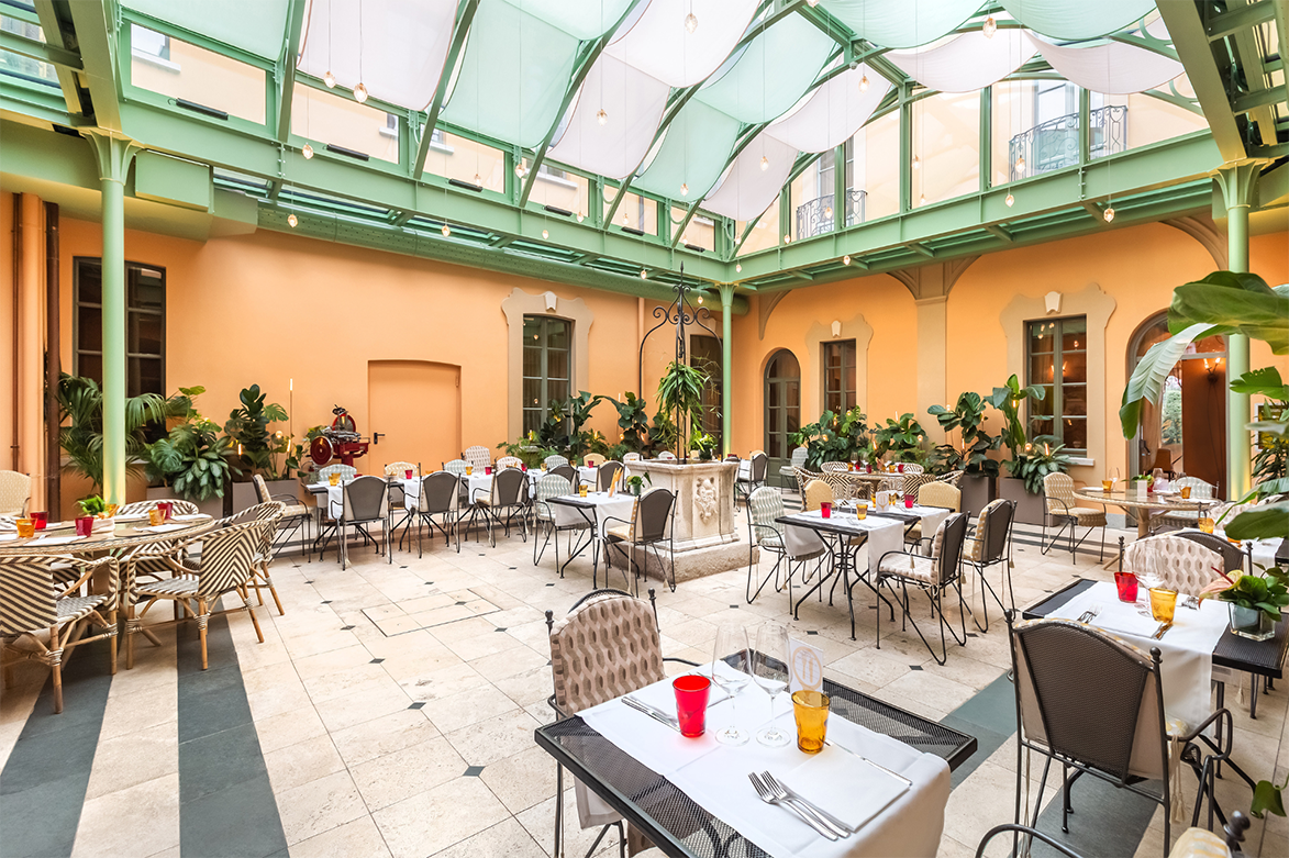 A spacious indoor courtyard restaurant with a glass glass ceiling orange walls and set tables